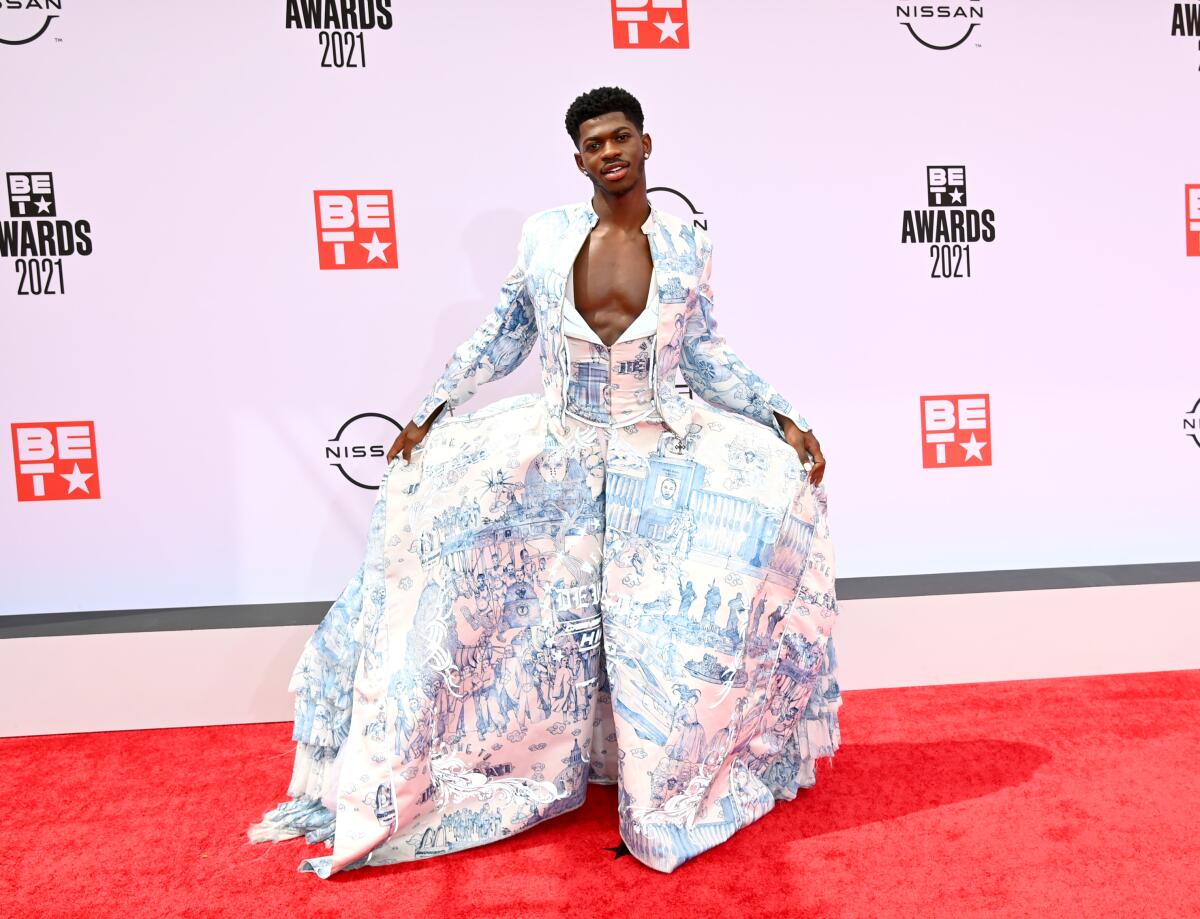 Lil Nas X wears a Cinderella-like blue and white gown with images of pople and buildings on the red carpet