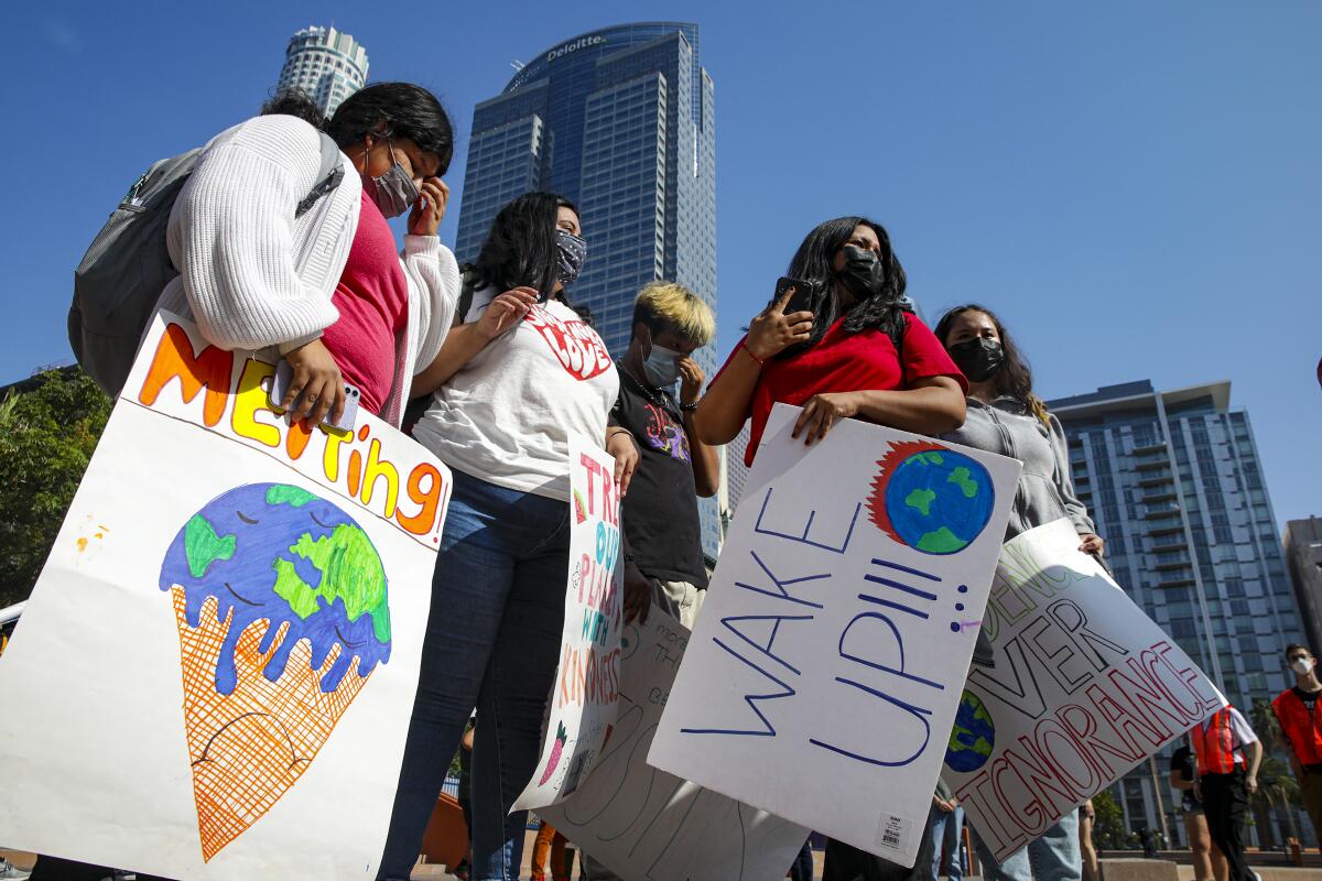 Students carry climate change protest signs with downtown L.A. buildings behind them