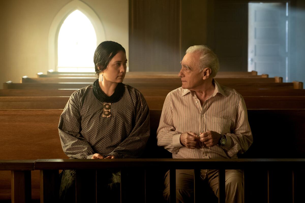 Lily Gladstone talks with Martin Scorsese sitting in a pew of a church.