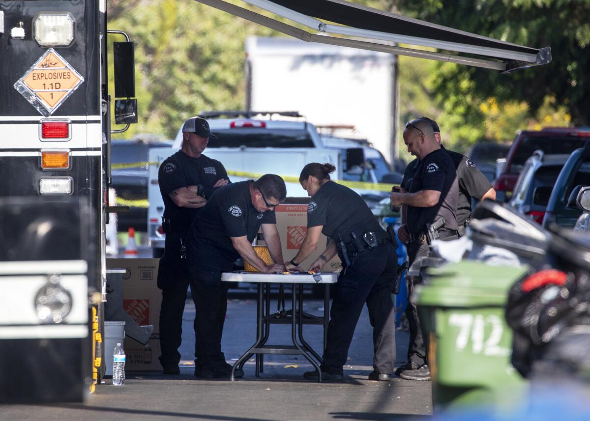 Police officers stand in shade of a police RV and look at something on a portable table.