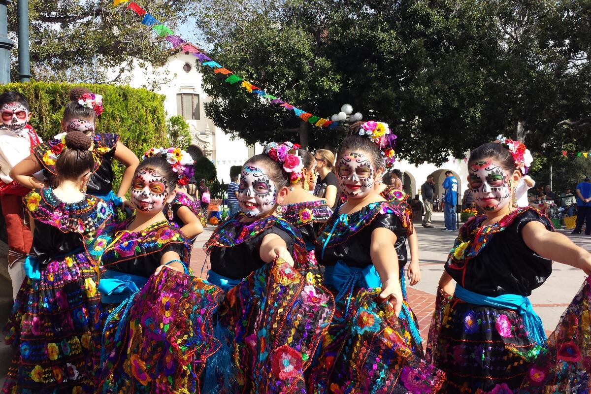 Four girls in traditional dresses with their faces painted as calaveras. 