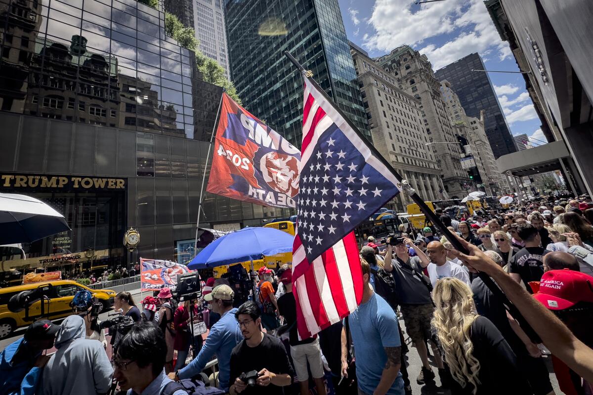 A hand is shown holding an inverted American flag in a crowd of people surrounded by skyscrapers