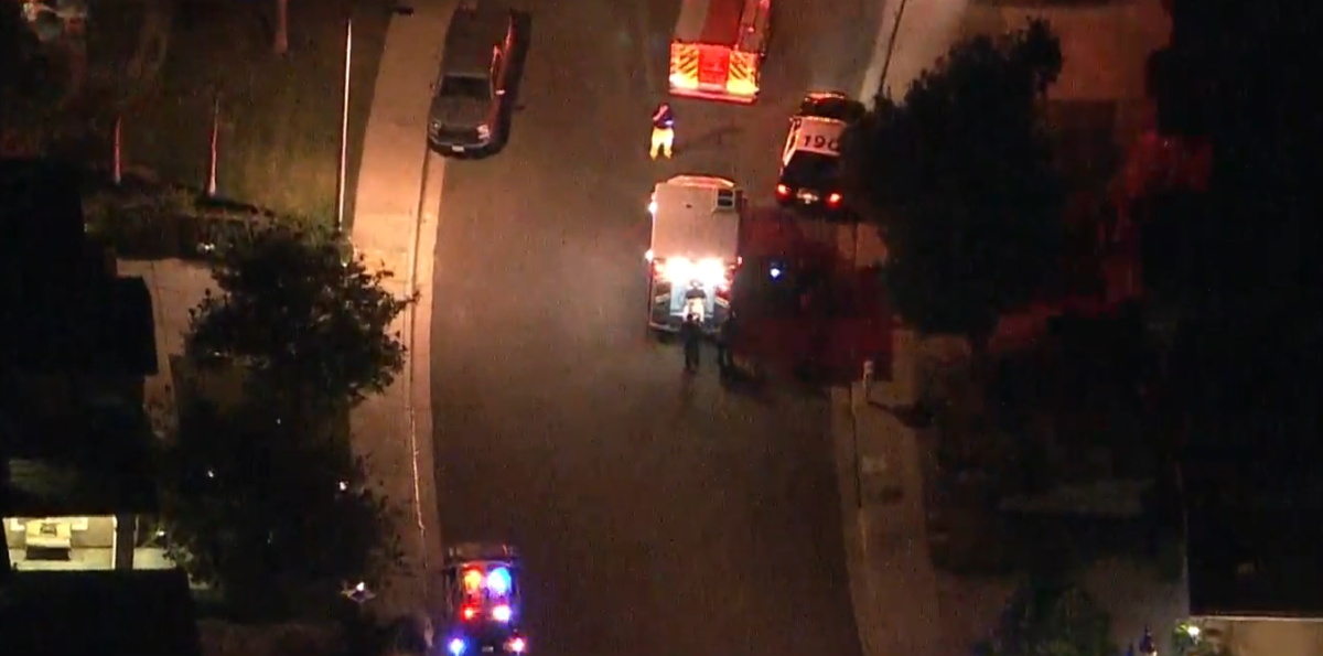 Aerial view of paramedics loading a man in a gurney into the back of an ambulance on a residential street at night