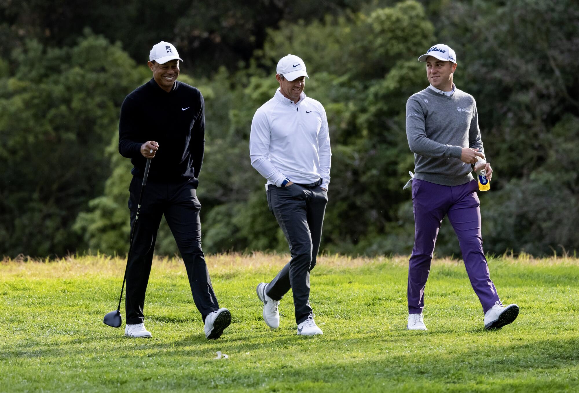Tiger Woods, left, and Justin Thomas, right, share a laugh while walking with Rory McIlroy