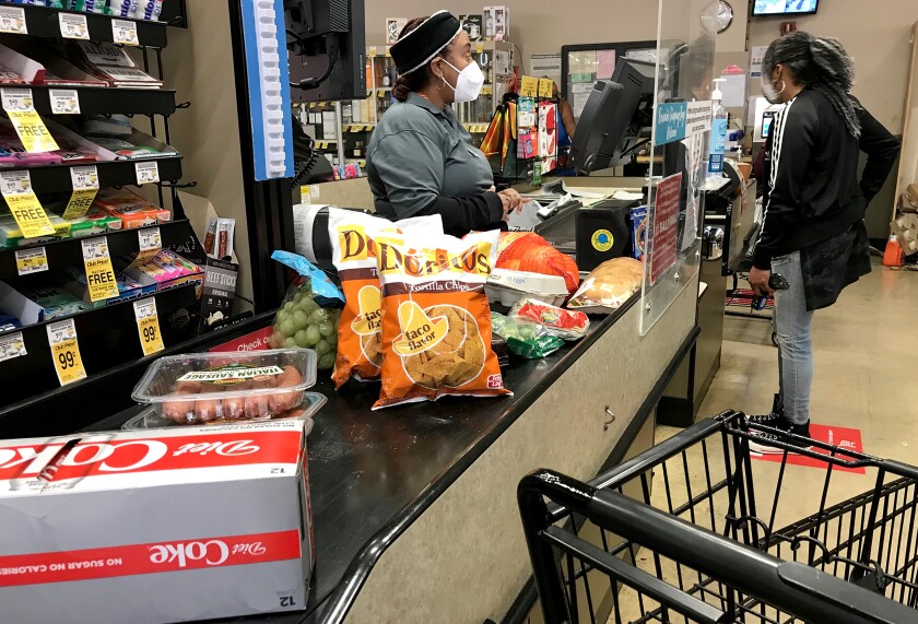  A masked cashier helps a customer in a grocery store checkout line