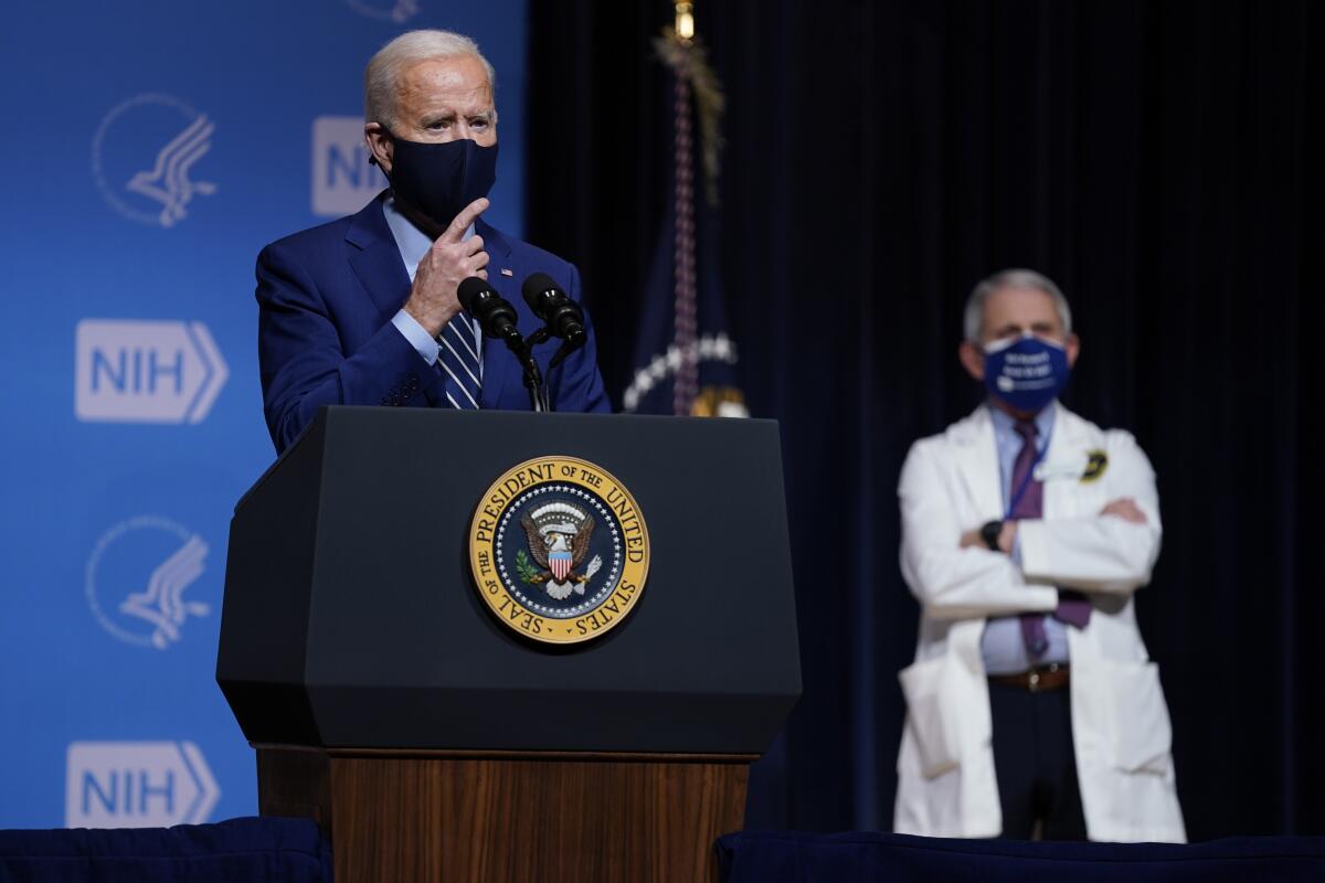 President Biden speaks as Dr. Anthony Fauci, right, listens in the background. 