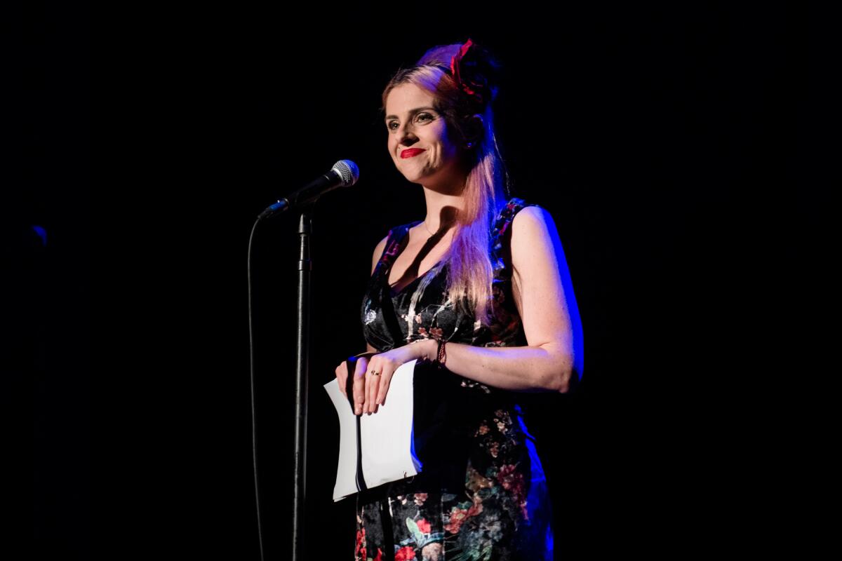 A woman at a microphone holds a script.