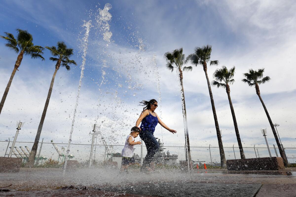 Olga Llamas, of Moreno Valley, with son Isaac Llamas, escape the heat while playing in a water fountain near the USS Iowa in San Pedro, Calif.