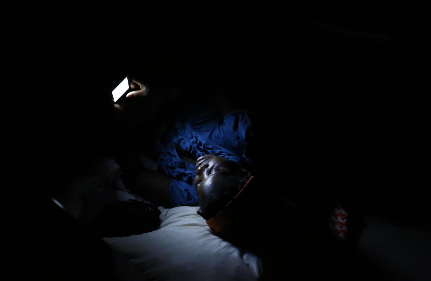 A Haitian woman checks her phone before going to sleep at the Desayunador Salesiano Padre Chava shelter. Women and children spread blankets on the floor in between the dining room tables to sleep atthe facility, which is filled to capacity.