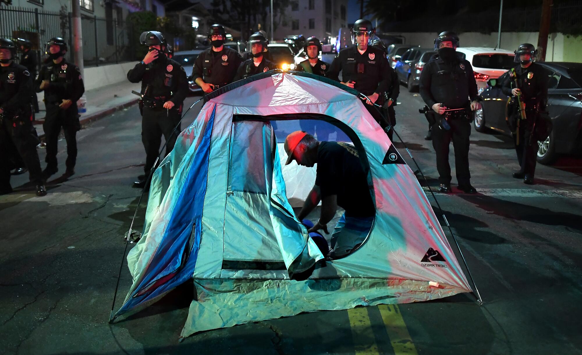 A protester sets up a tent in the street as LAPD officers stand guard 
