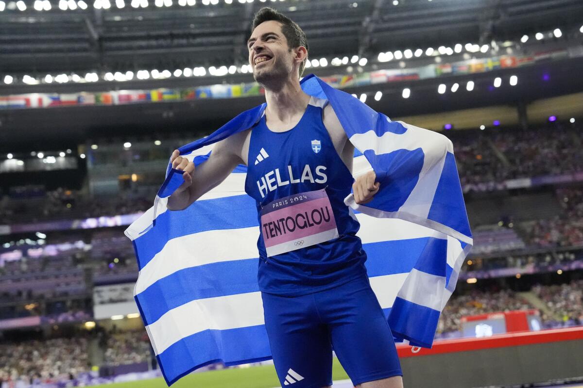 Miltiadis Tentoglou smiles with a Greek flag across his shoulders.