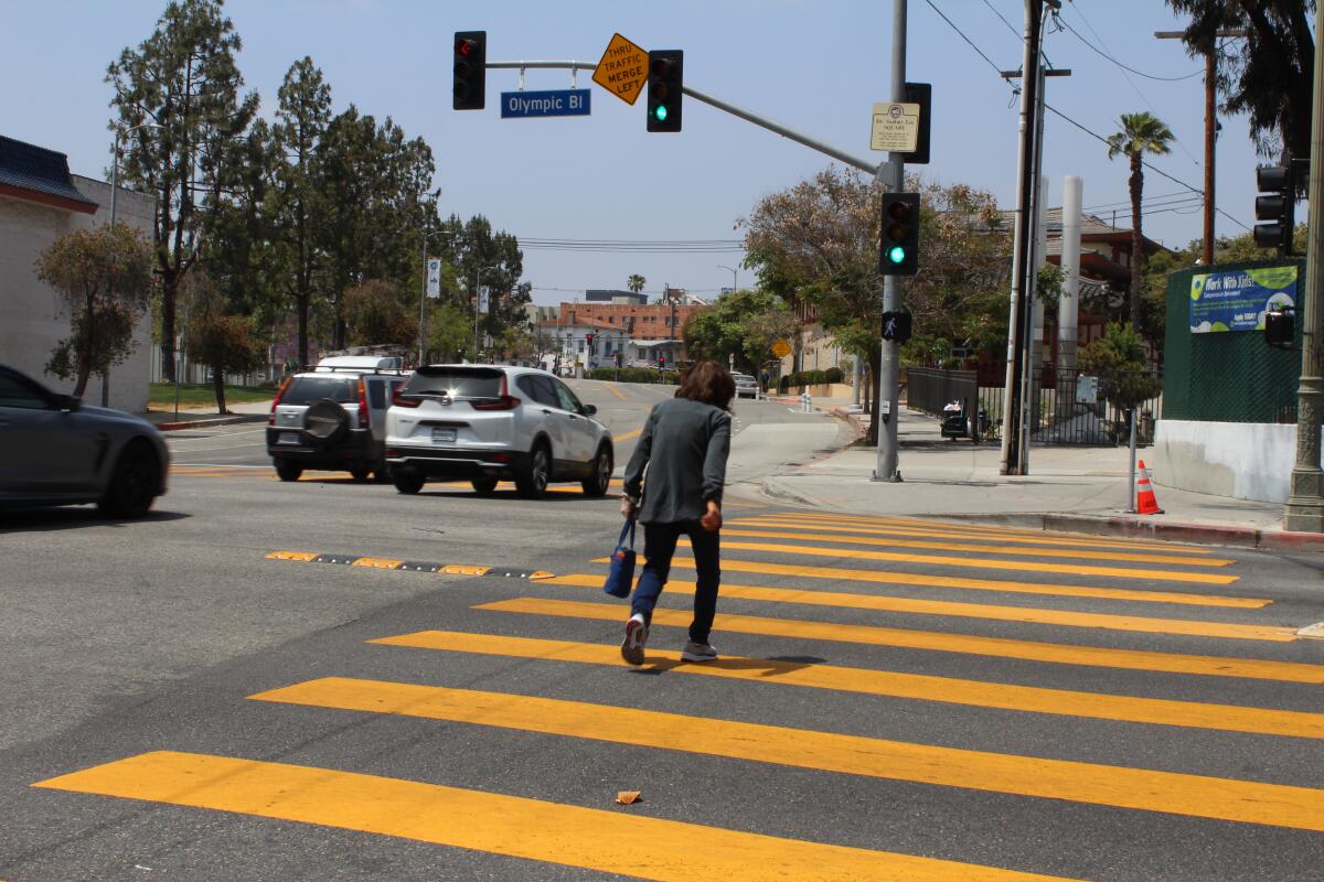 A woman walks in a crosswalk as cars drive by to her left.