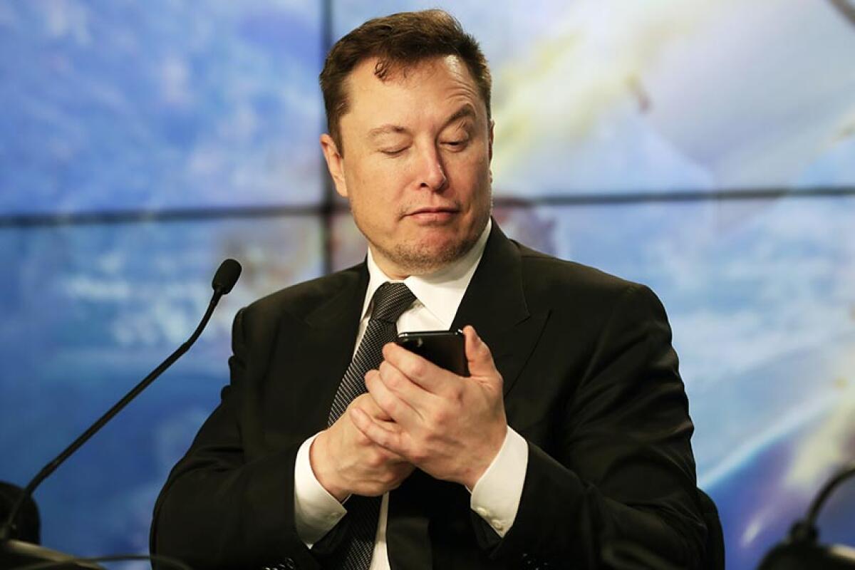 Elon Musk uses his smartphone while wearing a suit at a news conference at Kennedy Space Center