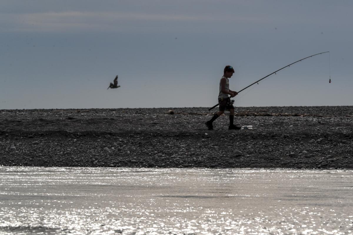 A young fisherman walks along a spit of land separating the Pacific Ocean and the Klamath River.