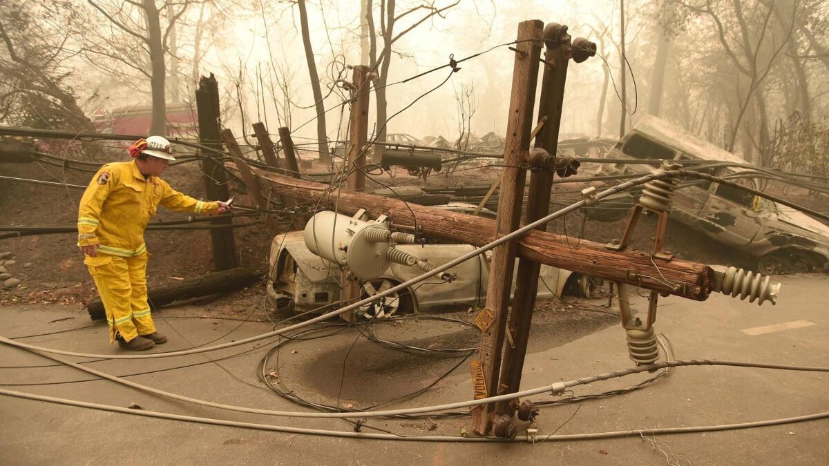 Firefighter Scott Wit surveys burned-out vehicles and a fallen power line after the Camp fire tore through Paradise, Calif., last year. PG&E's potential liability helped to prompt its bankruptcy filing Tuesday.