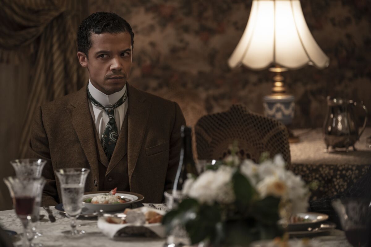 An early 20th century man seated at a fancy table in a brown suit.