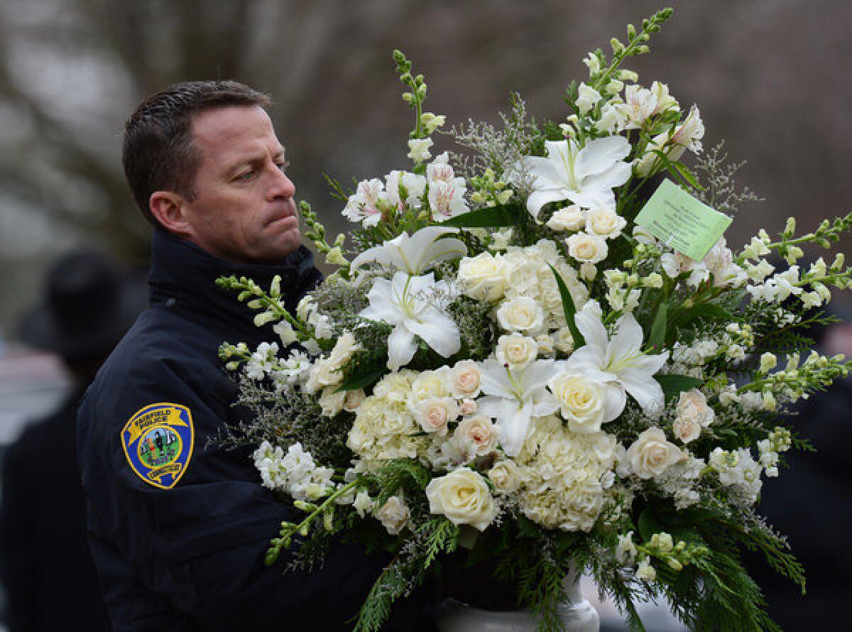 A police officer helps move floral arrangements after the funeral Monday of a boy who died in the shooting at Sandy Hook Elementary School. Shares of gun makers have tumbled in the wake of the tragedy.