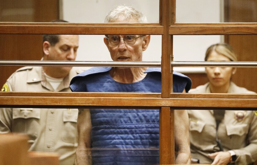 Ed Buck in a blue vest in a courtroom, with two deputies standing behind him