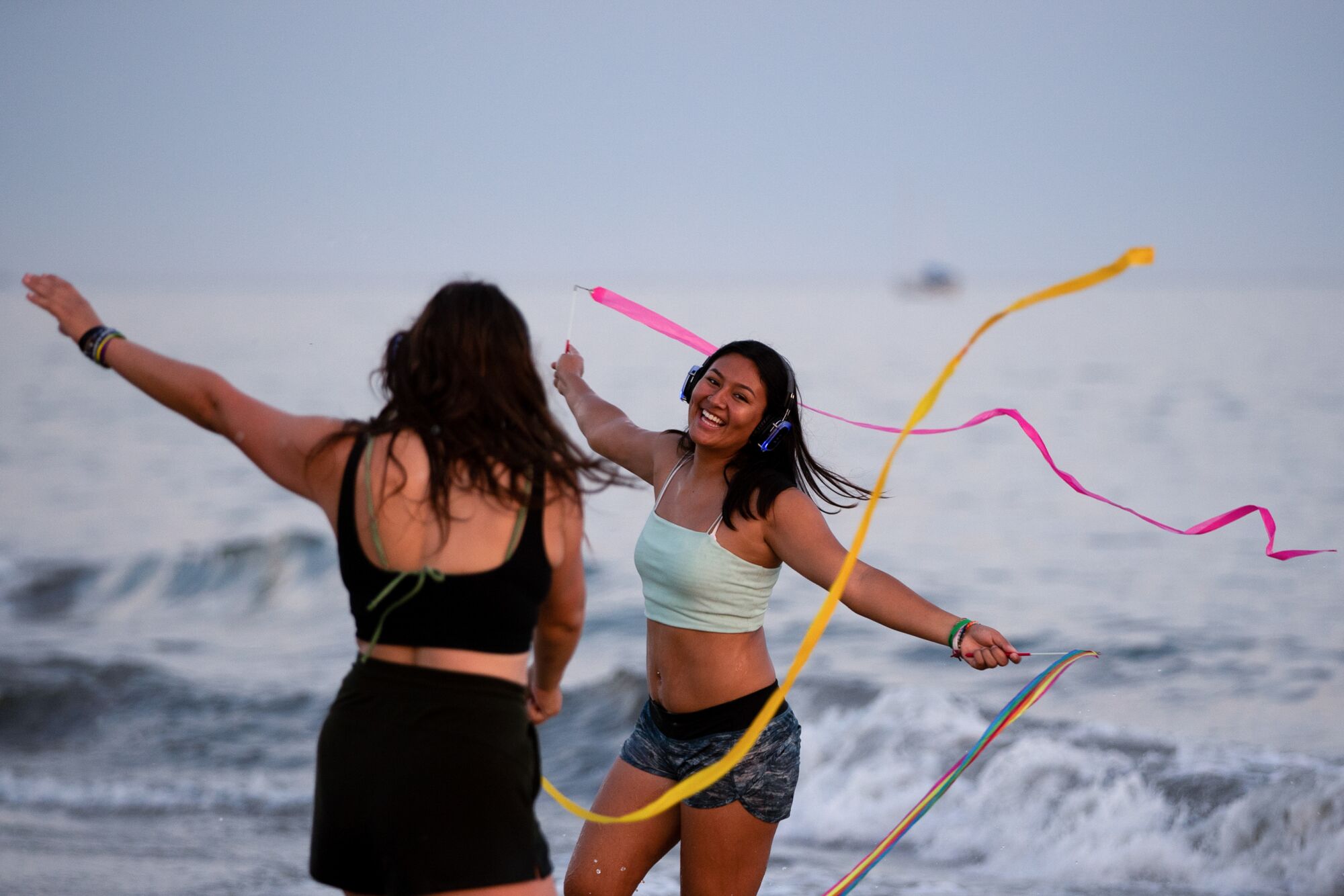 Two young women waving multicolored streamers while dancing by the ocean.