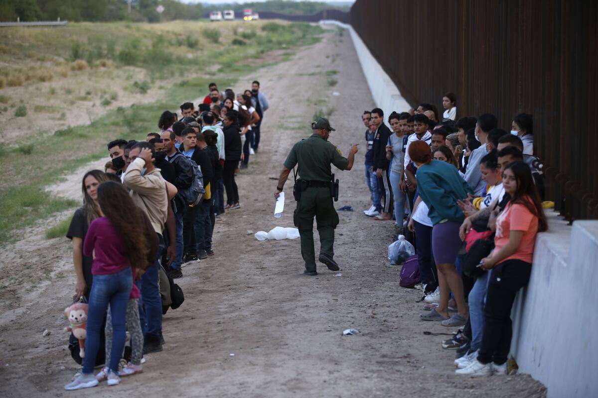 ARCHIVO - Un grupo de migrantes permanecen junto al muro de la frontera con México
