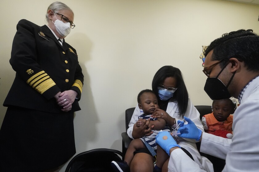 A doctor holds her nine-month-old son on her lap as another doctor administers a vaccine.