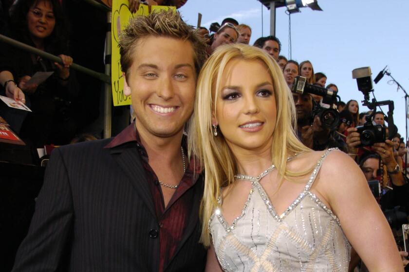 Lance Bass is dressed in a black suit and is posing together with Britney Spears who is wearing a silver dress