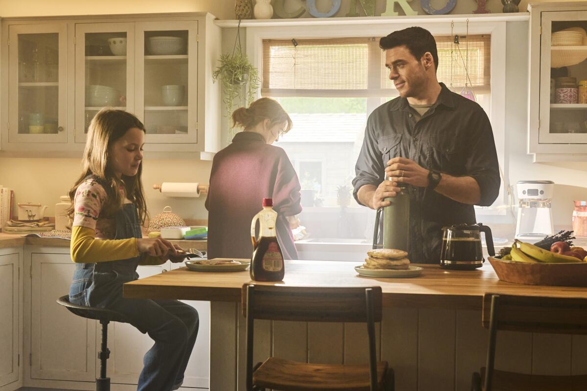 A man stands with a woman and child in a sunny kitchen.