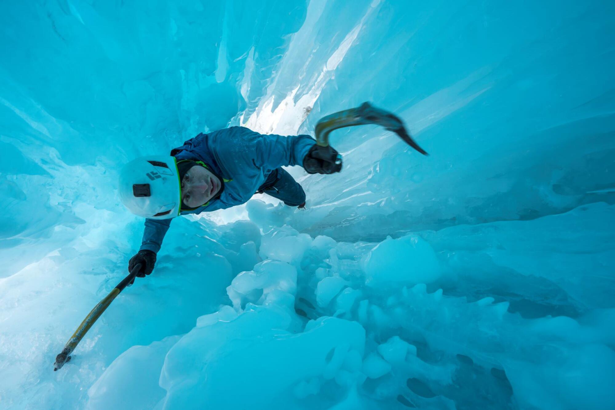 A young man uses an ice pick to climb up a glacier