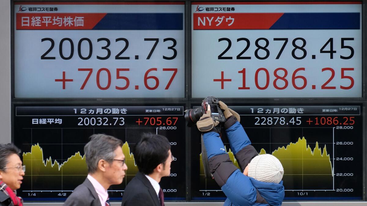 Pedestrians in Tokyo pass a board showing figures for the Tokyo and New York stock exchanges.