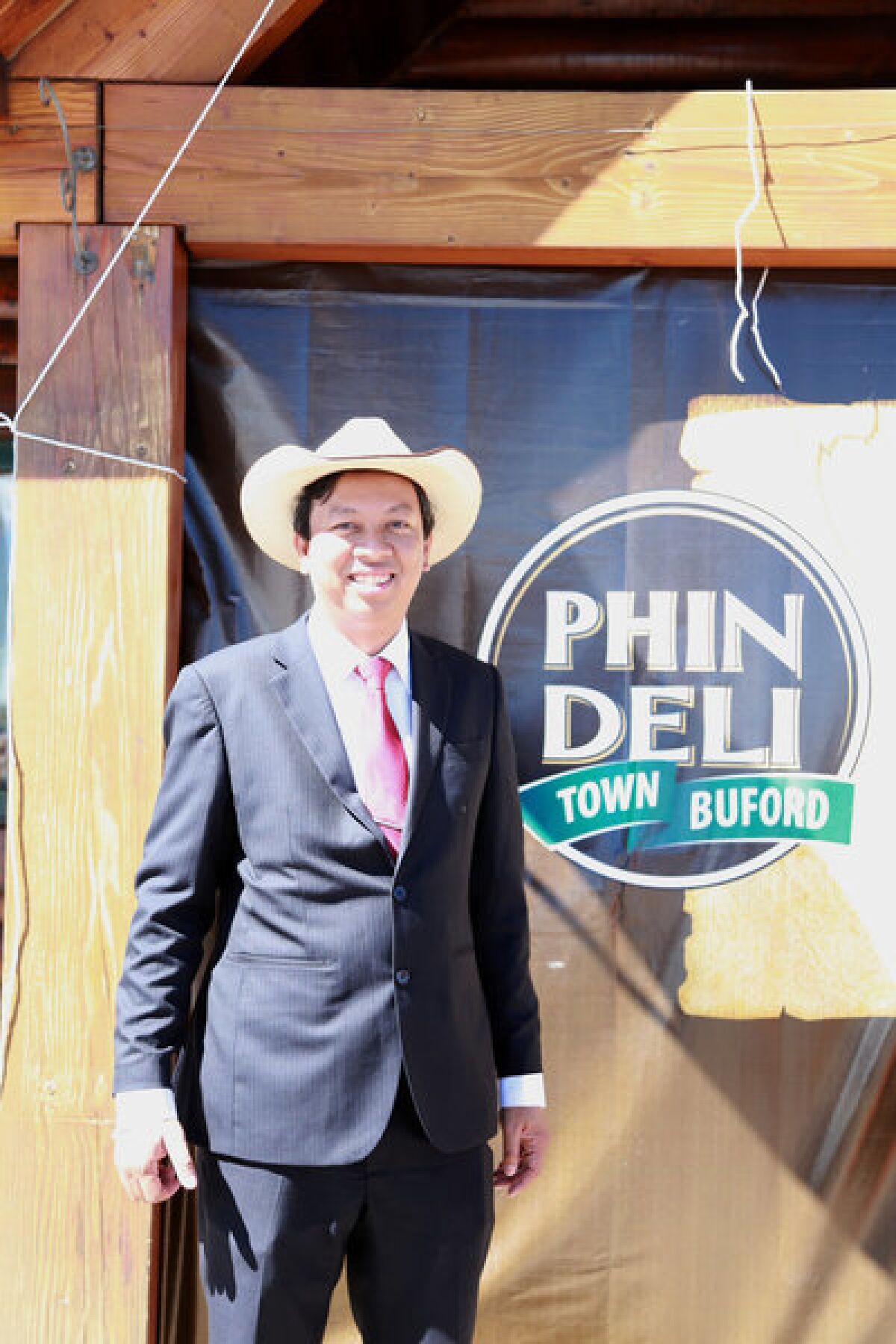Town owner Pham tries out some Wyoming wear in front of a sign for his PhinDeli coffee. The name PhinDeli translates to "delicious filter coffee."