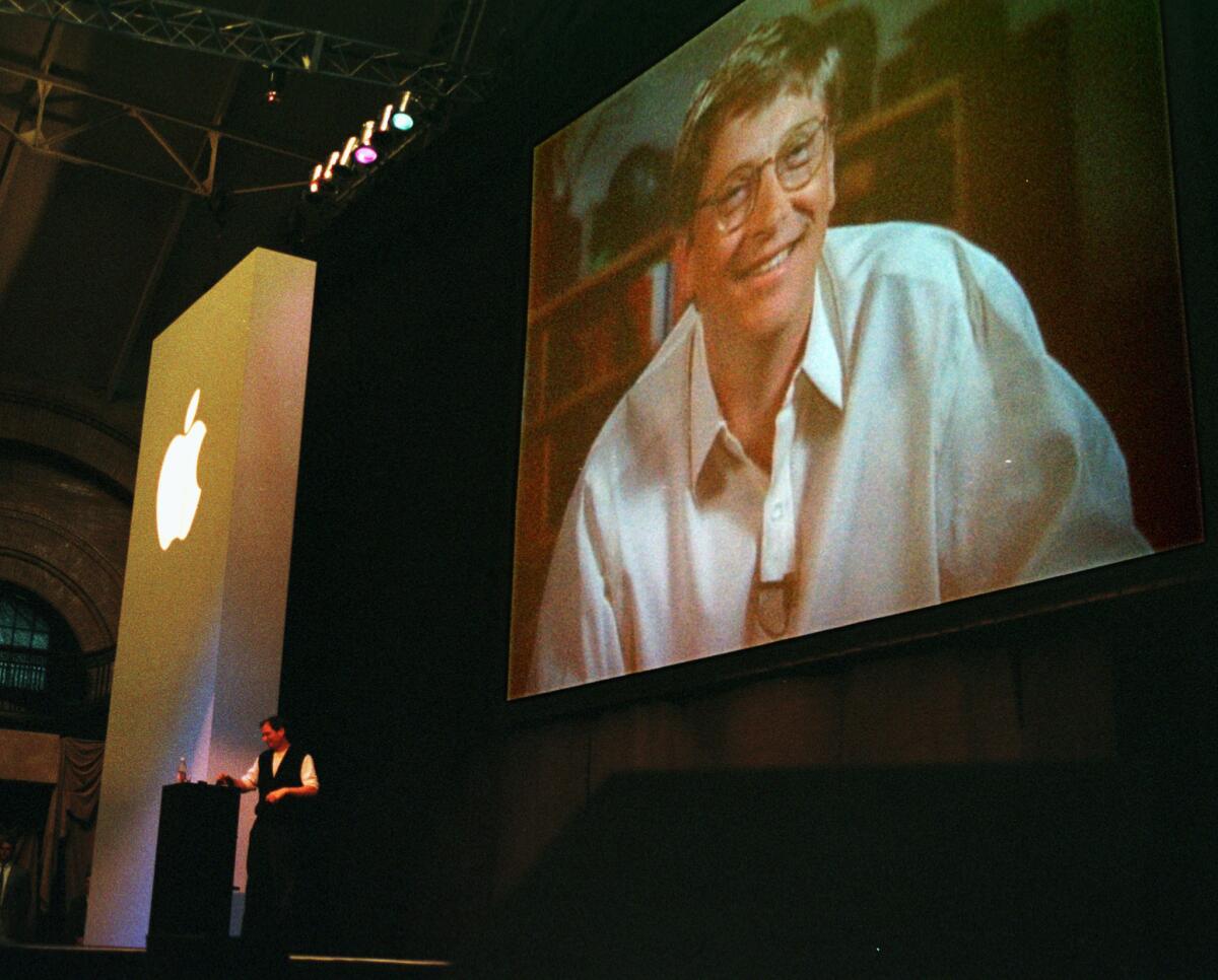 In 1997, Apple interim Chief Executive Steve Jobs, seen at the podium, had a big surprise for Macworld attendees: Rival Microsoft had thrown Apple a lifeline by agreeing to invest $150 million to keep the company afloat. As the announcement is made, a gigantic image of Microsoft CEO Bill Gates appears on a video screen behind Jobs, as the audience gasps.