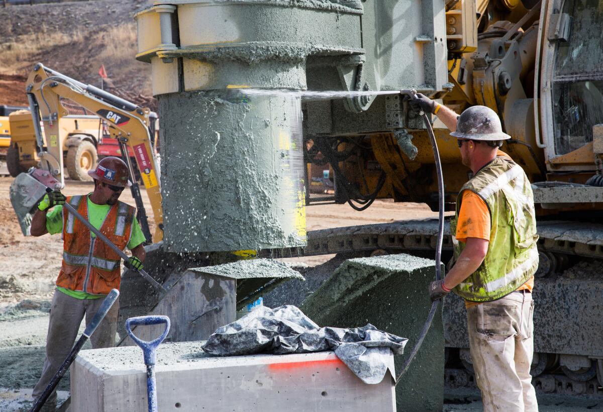 Workers clean the bit of a drilling rig used for drilling holes at the cutoff wall downslope of the Lake Oroville emergency spillway on Aug. 14.
