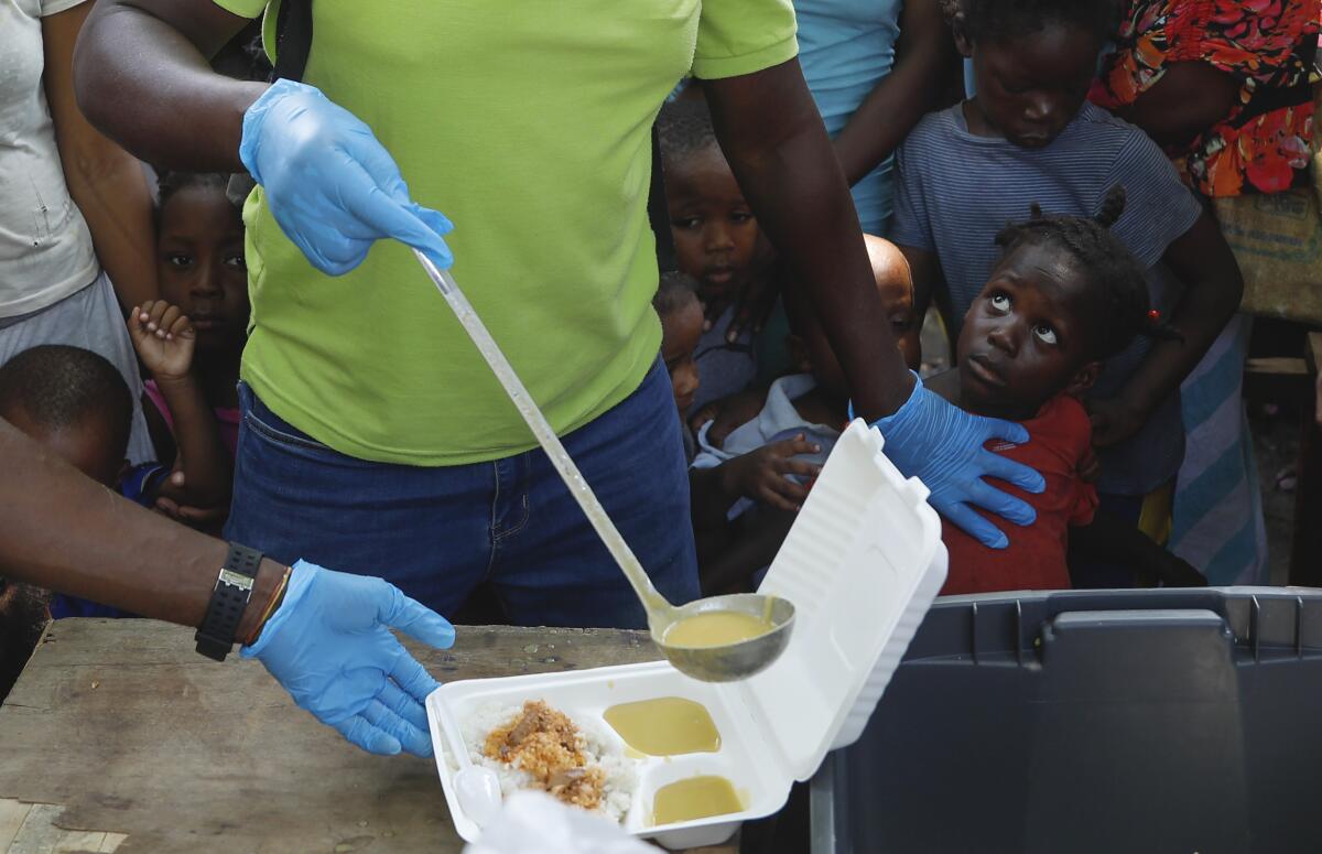 A server ladles soup into a container as children line up to receive food.