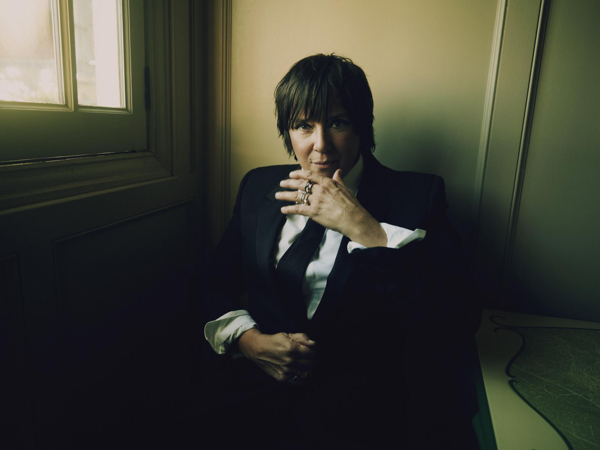 Cat Power with a shag cut sits in a corner, one hand raised to her chin. 
