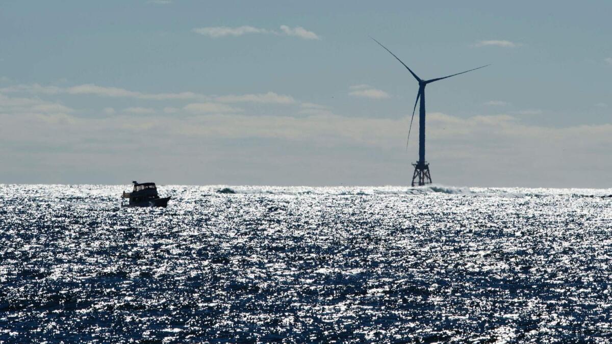 A vessel floats near a wind turbine amid ocean waves.