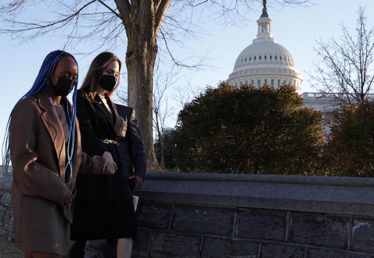 Two women in masks walk outdoors with the U.S. Capitol in the background