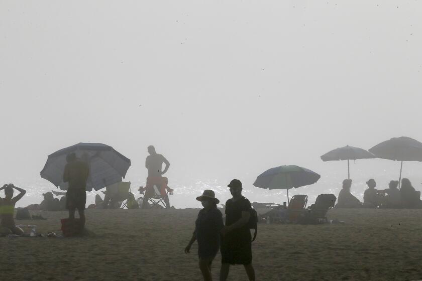 HUNTINGTON BEACH, CALIF. - APR. 25, 2020. Beachgowers set up on Huntington Beach, where afternoon fog and cool temperatures limited the number of visitors to Orange County beaches on Saturday, April 25, 2020. More people were expected to go to the coast to escape record high heat in some inland areas. Beaches in neighboring Los Angeles County remain closed because of the coronavirus pandemic. (Luis Sinco/Los Angeles Times)