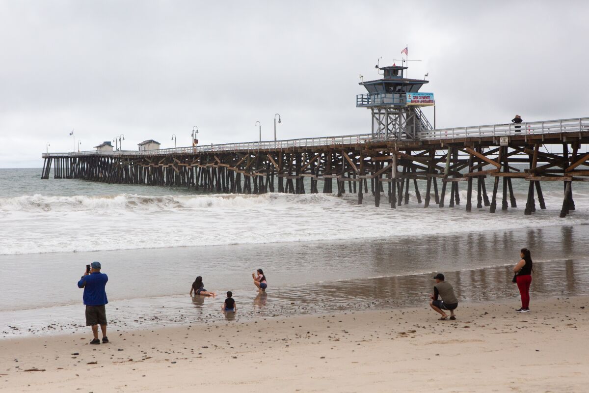 Families practice social distancing while playing near the San Clemente Pier on Monday.