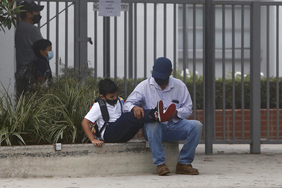 A parent fixes his son's shoelaces as students arrive for class at Rea Elementary School in Costa Mesa on Tuesday morning.