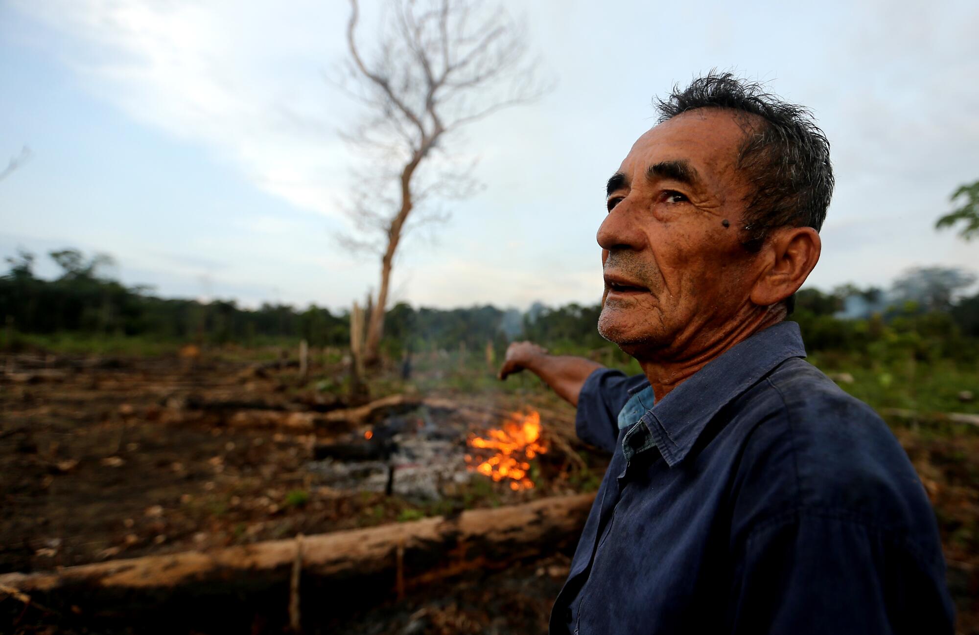 A man stands near cleared land where a small fire is burning . 