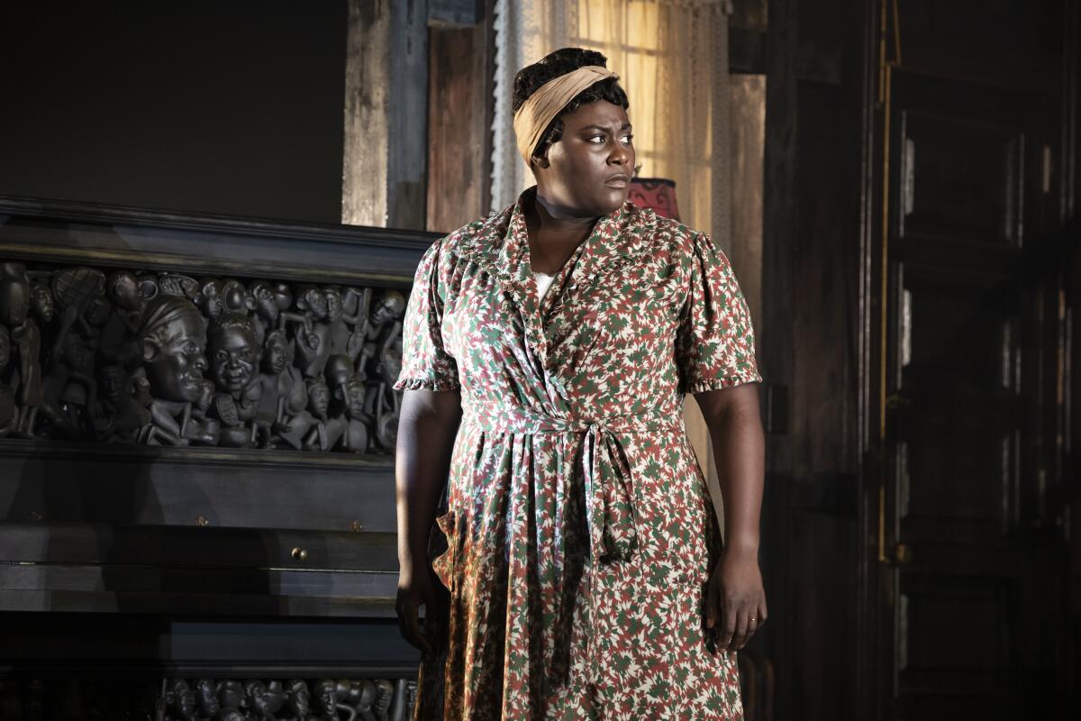 A woman stands in front of a richly carved piano.