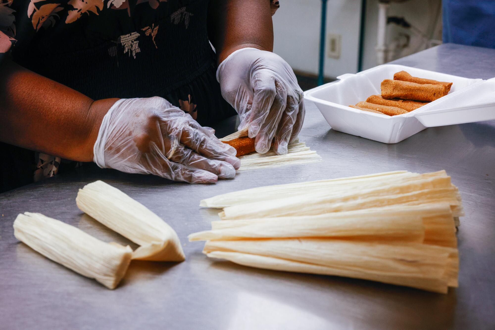 A person wearing gloves on their hands rolls tamales.