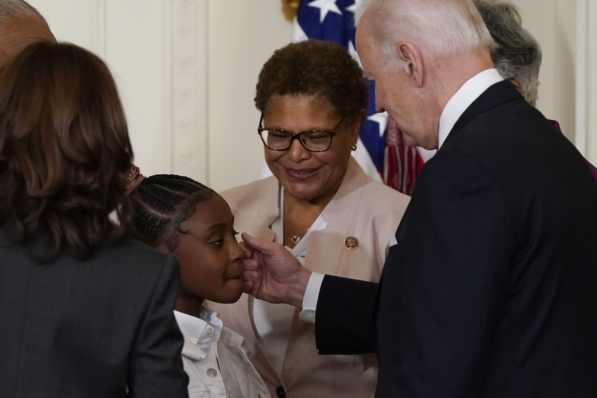 President Biden touches a little girl's cheek as Rep. Karen Bass smiles.
