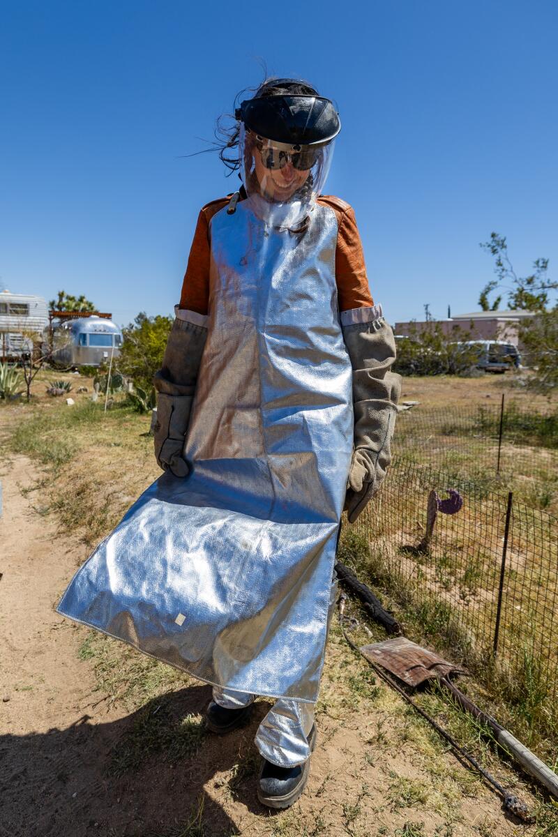 A woman walking in the desert wears a protective apron and clear mask.
