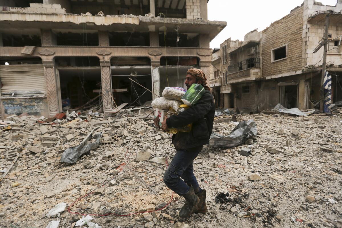 A man carries belongings through a street destroyed by a Syrian government offensive in Sarmin, Idlib province