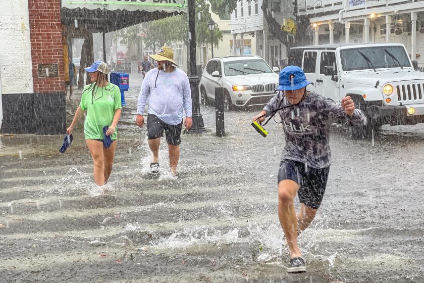 Pedestrians dash across the intersection of Greene and Duval streets as heavy winds and rain associated with Tropical Storm Elsa passes Key West, Fla., on Tuesday, July 6, 2021. The weather was getting worse in southern Florida on Tuesday morning as Tropical Storm Elsa began lashing the Florida Keys, complicating the search for survivors in the condo collapse and prompting a hurricane watch for the peninsula's upper Gulf Coast. (Rob O'Neal/The Key West Citizen via AP)