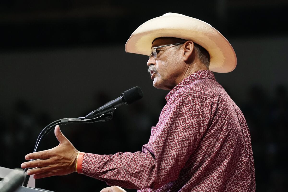 Mark Finchem, wearing a cowboy hat, gestures with his hand and speaks into a microphone. 