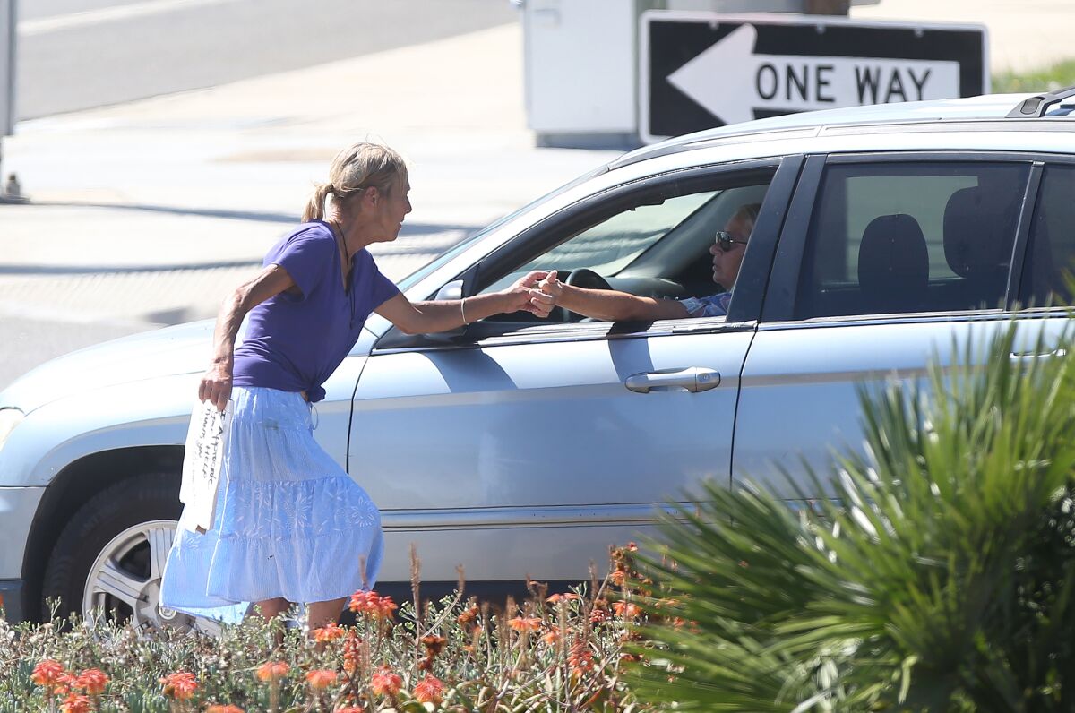 A woman accepts a driver's donation Tuesday at the traffic signal where Newport Boulevard meets West Coast Highway.