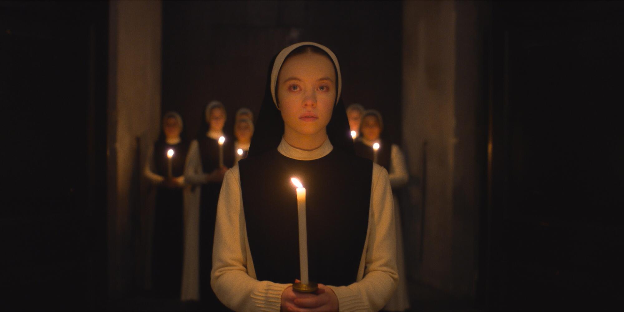 A nun in a convent holds a candle.