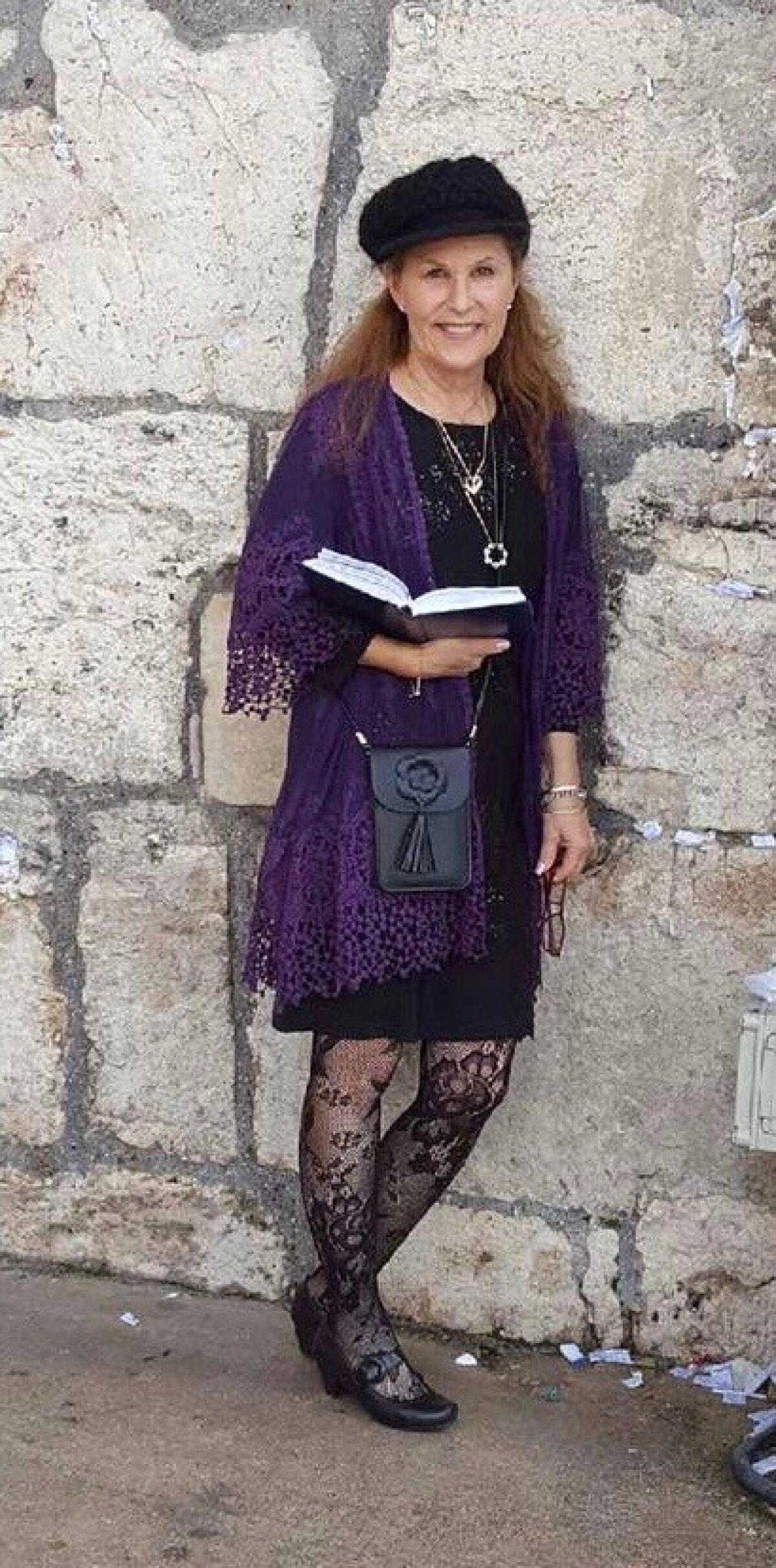 An undated photo of Lori Gilbert-Kaye leaning against a wall outside and holding an open book